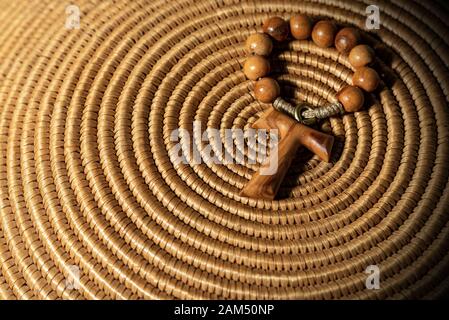 Tau, wooden cross in shape of the letter t (religious symbol of St. Francis of Assisi) with rosary bead, on brown woven wicker texture Stock Photo