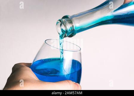 Pouring alcohol from a bottle into a glass goblet on a white background. Glass of wine and a bottle with pouring liquid. A stream of blue flows from t Stock Photo