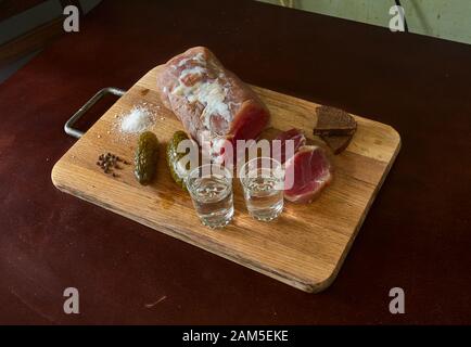 Vodka with raw meat, salt cucumber on wooden meat cutting board. Stock Photo