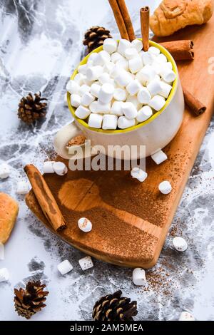 a cup of Christmas New Year delicious hot chocolate and cocoa with marshmallows sprinkled with cocoa powder, cones and croissants, cinnamon on a gray Stock Photo