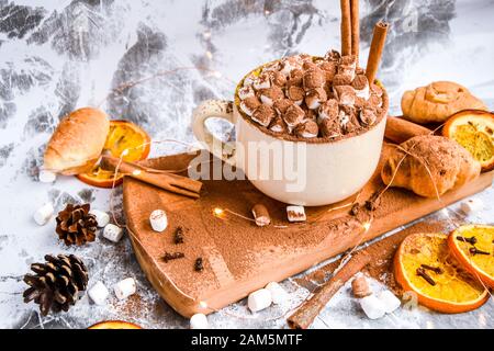 a cup of Christmas New Year delicious hot chocolate and cocoa with marshmallows sprinkled with cocoa powder, cones and croissants, cinnamon on a gray Stock Photo