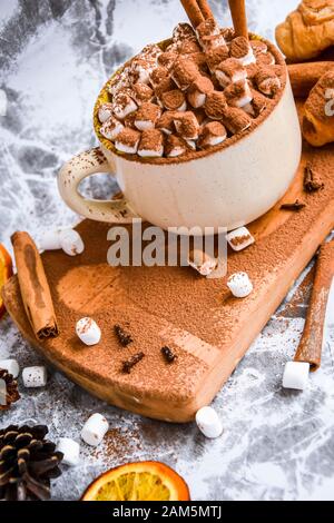 a cup of Christmas New Year delicious hot chocolate and cocoa with marshmallows sprinkled with cocoa powder, cones and croissants, cinnamon on a gray Stock Photo