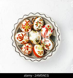 Ukrainian Easter eggs decorated with wax-resist dyeing technique. Pysanky in a bowl, top view, white background Stock Photo