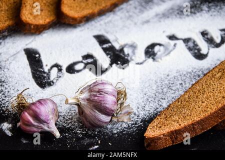 Inscription bakery on white wheat flour scattered Sliced rye bread with garlic on dark background Stock Photo