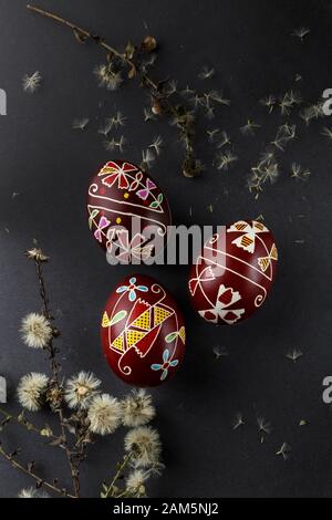 Pysanky, Ukrainian Easter eggs decorated with wax-resist dyeing technique, dry flowers on black background Stock Photo
