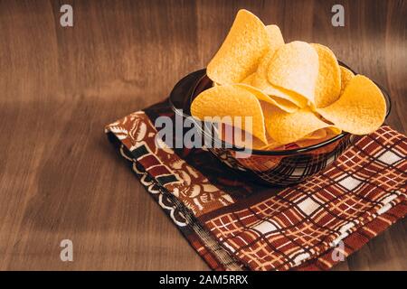Crispy potato chips in bowl on wooden background, with kitchen towel Stock Photo