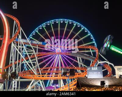 London, England, UK - December 28, 2019: Front view of Ferris wheel and rollercoaster at night in winter wonderland in Christmas holiday