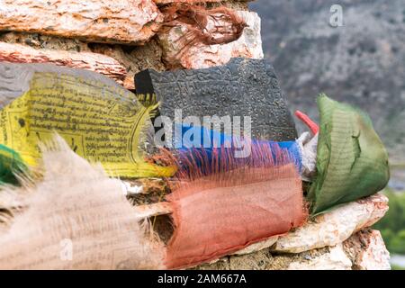 Mani stones with inscribed Buddhist mantras and colorful prayer flags in Marpha village, Mustang district, Nepal Stock Photo
