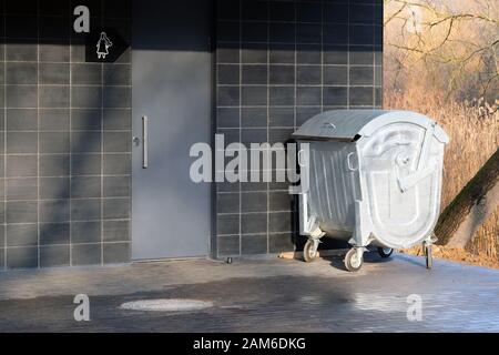 Entrance to the public toilet in the city park and a metal litter bin. The door to the building and the trash can at the entrance. Stock Photo