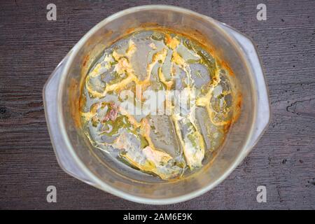 Glass baking dish with grease and leftover food. Glass baking dish after cooking fatty meat top view. Dirty kitchen utensils on a wooden background. Stock Photo