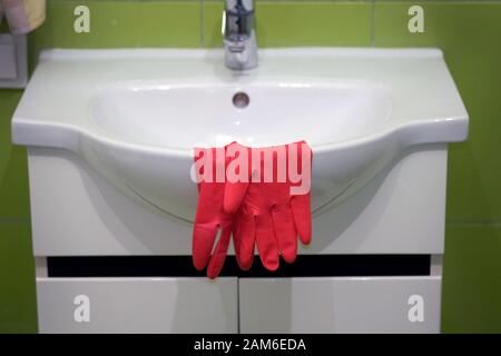 Red rubber gloves on a white washbasin in the bathroom. Cleaning in the bathroom. Stock Photo