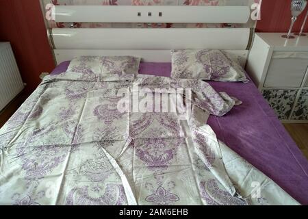 Bed in the bedroom with a colored sheet. White bed with two pillows and wrinkled sheets. Stock Photo