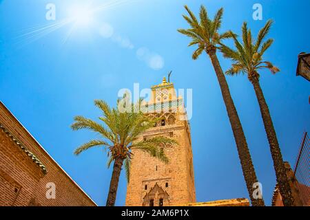 Tower of Koutoubia Mosque minaret at medina quarter of Marrakesh, Morocco. There is beautiful green palms. Blue sky is in the background. Stock Photo