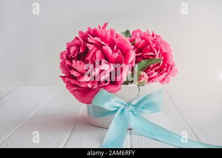 Close up beautiful pink peony flower bouquet in round box with turquoise sattin ribbon bow on white wooden background. Gift, greeting, compliment idea Stock Photo