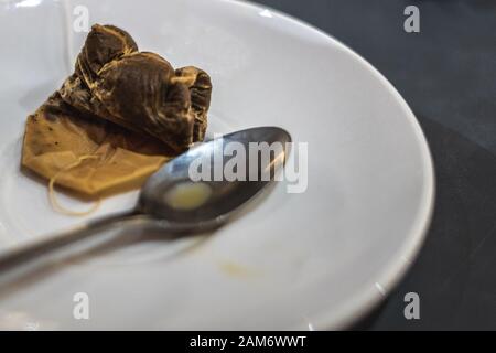 a used tea bag on a white saucer next to a dirty teaspoon Stock Photo