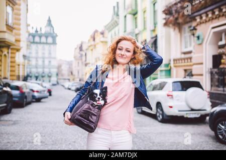pet owner use Pet Travel Carrier inside with a chihuahua dog. Dog Carry Bag on the shoulder of a caucasian red-haired woman in a European city Stock Photo