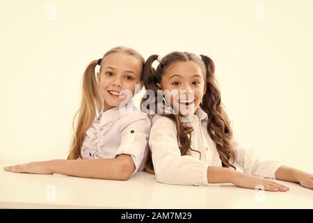 First grade. Happy childhood. Adorable schoolgirls. Back to school. Education concept. Beautiful girls best friends. Formal style. Schoolgirls sit desk white background. Schoolgirls emotional friends. Stock Photo