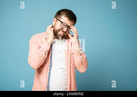 Bearded man is tired or suffering from a headache. He closed eyes and bared teeth. Stock Photo
