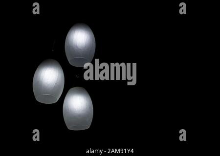 Three bright led residential light bulbs illuminate a dark room on black background. Business, goal setting, energy saving concepts. Stock Photo