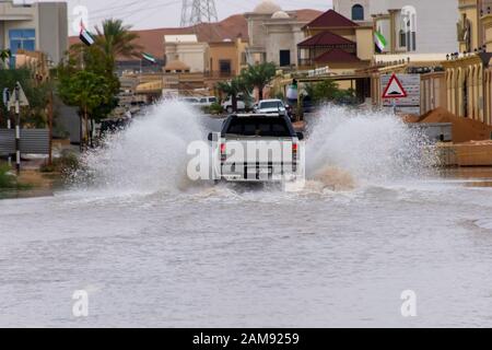 Truck driving through flood waters on the street making large splashes of water in a residential area. Stock Photo