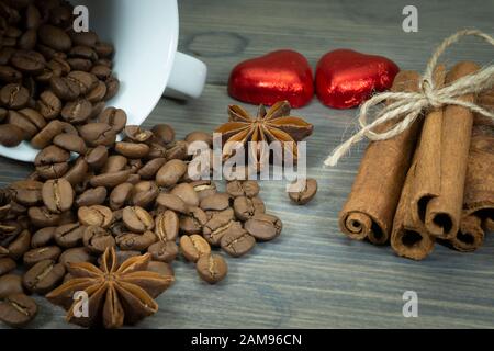 Roasted coffee beans spilling from a cup, cinnamon with star anise spice on a rustic wooden table in a close up view Stock Photo