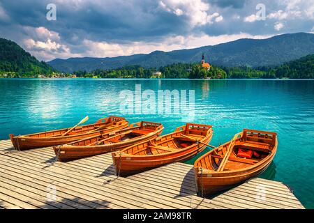 Old wooden rowing boats moored at the pier on the lake Bled. Gorgeous Pillgrimage church and small island in background, Bled, Slovenia, Europe Stock Photo