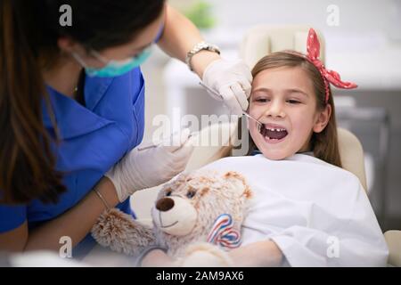 Caring dentist examining her patient teeth while she holds her teddy bear Stock Photo