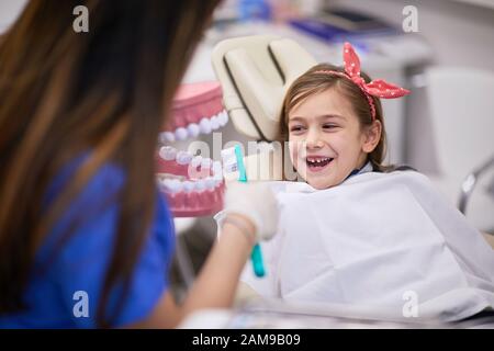 Education in dental office, correct teeth brushing, smiling girl Stock Photo