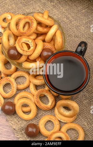 Small bagels, chocolates, a mug of tea and a rough homespun cloth on a wooden background close-up Stock Photo
