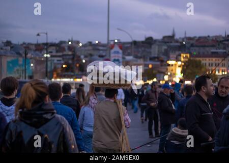 Bagel salesman among people. He carries the bagels on his head. Photographed in the evening. Photographed on the Galata Bridge. Stock Photo