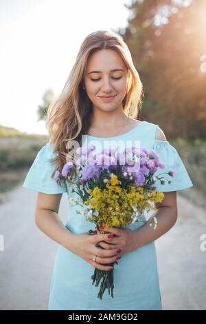 A beautiful girl is standing with a bouquet in her hands. The sun is breaking through her shoulder. Stock Photo