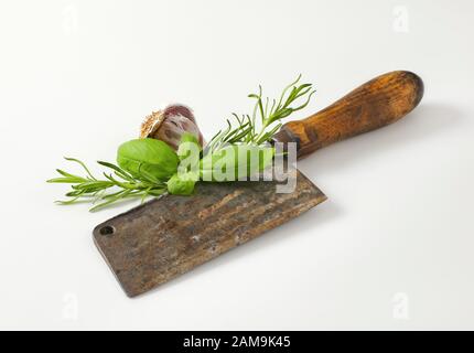Old rusty meat cleaver knife with fresh basil and rosemary Stock Photo