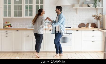 Happy family couple dancing barefoot on wooden floor in kitchen. Stock Photo