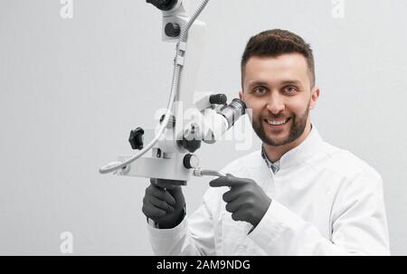 Front cropped view of professional dentist on white isolated background. Smiling doctor in white uniform and black gloves keeping equipment, looking at camera and posing. Concept of stomatology. Stock Photo