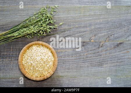 Oatmeal flakes in a bamboo bowl with green oats on an old faded gray wooden table background. The concept of cooking natural healthy food. Stock Photo
