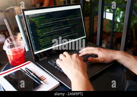 Developer programmer with laptop. Program code and script data on screen. Young freelancer in glasses working on project in cafe. Back view over the Stock Photo