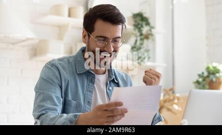 Happy young man reading paper letter with good news. Stock Photo