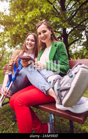 Two best friends, one with an injured leg, reading a book Stock Photo