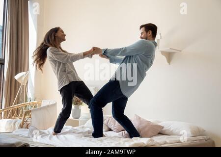 Overjoyed young family couple dancing to favorite music on bed. Stock Photo