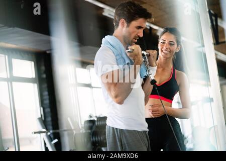 Sporty man doing weight exercises with assistance of her personal trainer Stock Photo