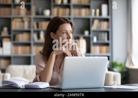 Pensive young woman distracted from work thinking Stock Photo
