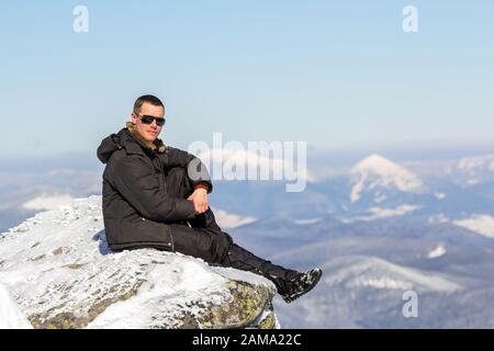 Silhouette of alone tourist sitting on snowy mountain top enjoying view and achievement on bright sunny winter day. Adventure, outdoors activities, he Stock Photo