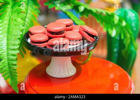 Red Macaroons. Several strawberries-flavored pink macaroons on a white and black ceramic tray. Children's party decoration with the detective theme. S Stock Photo