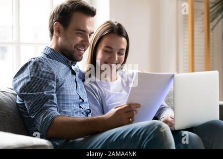 Young couple sit on couch paying bills online Stock Photo