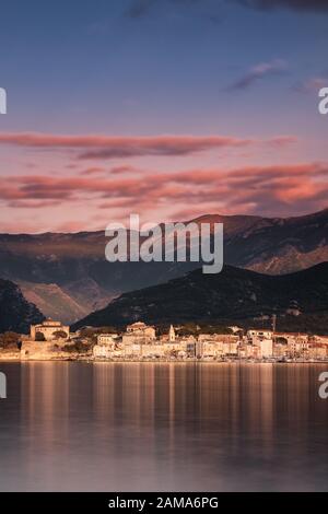 Evening sunshine lighting up the citadel and buildings of Saint Florent on the coast of Corsica with mountains behind Stock Photo