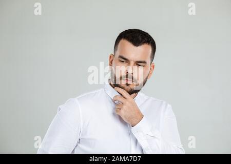 portrait of doubtful bearded man in white shirt asking questions on gray background. copy space Stock Photo