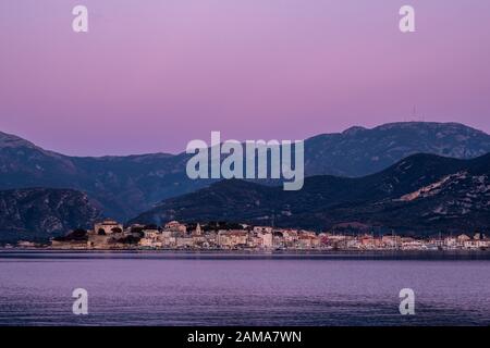 Dusk falling over the citadel and buildings of Saint Florent on the coast of Corsica with mountains behind Stock Photo