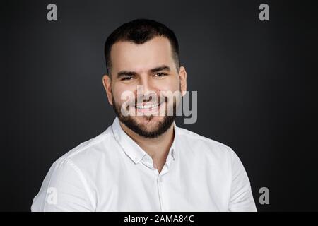 Close-up portrait of smiling handsome bearded man looking at camera on black background Stock Photo