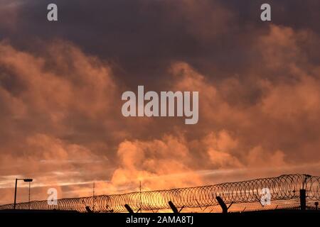 strange orange clouds in the sky over suffolk England, over razorwir fence looking like the sky is burning Stock Photo