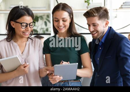 Three diverse colleagues discuss common task or project using tablet Stock Photo